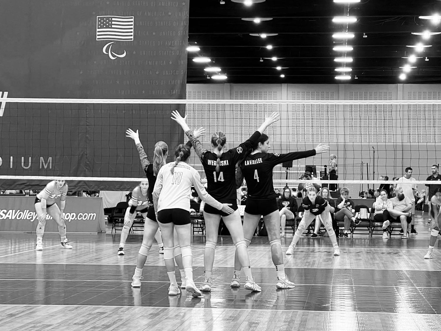four girls standing by volleyball net three with hands up